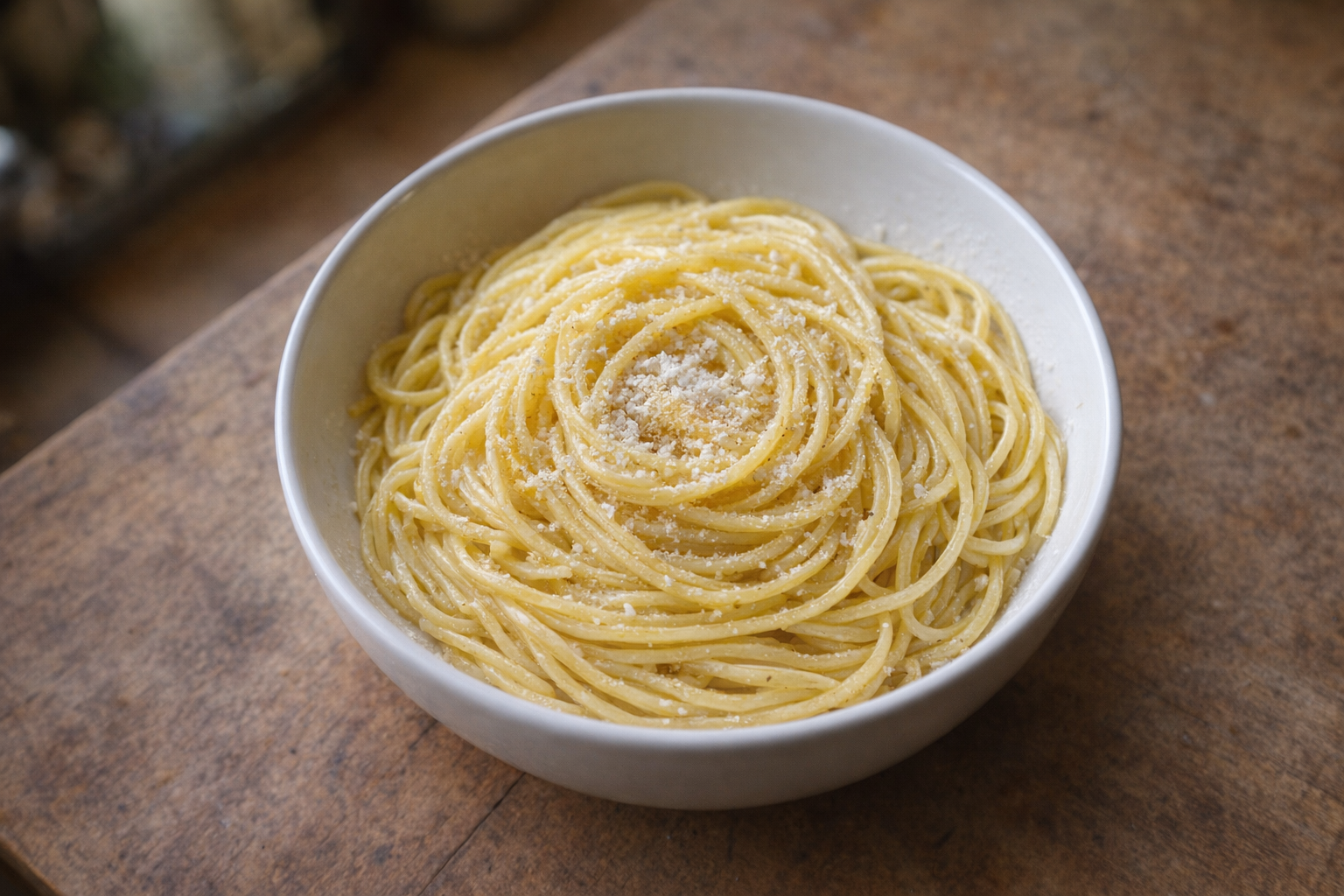An overhead shot of perfectly cooked spaghetti, glistening with olive oil and lightly sprinkled with Parmesan cheese, arranged artfully in a white bowl against a rustic wooden background with soft, natural light